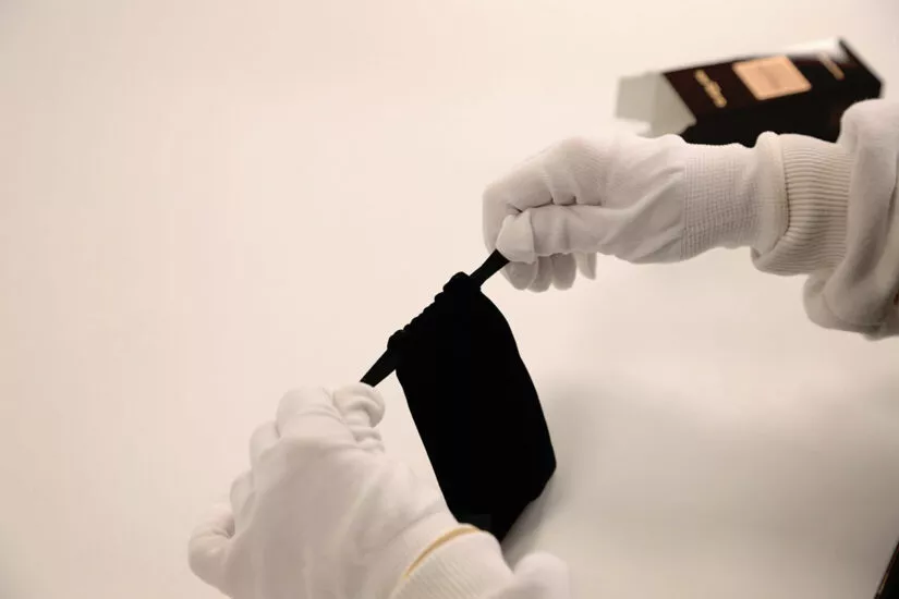 Mise en suédine d'un pinceau par une personne portant des gants blancs, symbolisant un emballage luxueux