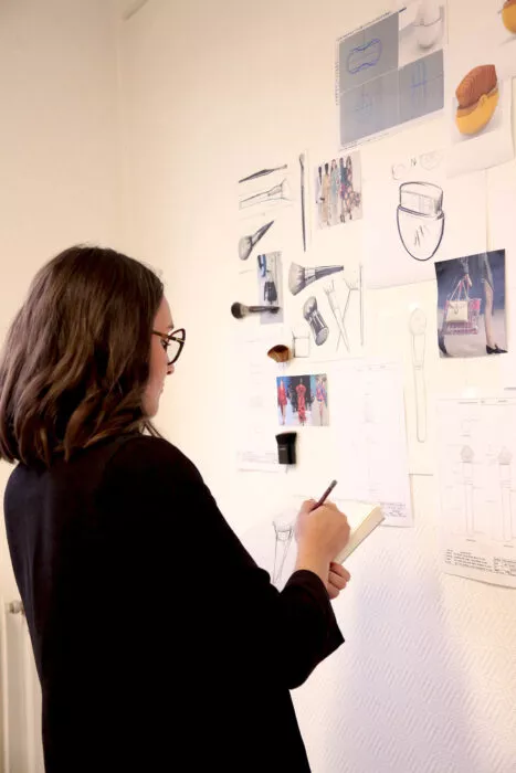 Femme dessinant des pinceaux sur carnet face à un mur de croquis