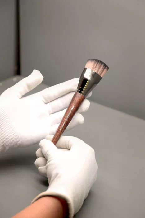 Présentation d’un pinceau maquillage haut de gamme avec manche en bois, manipulé avec des gants blancs