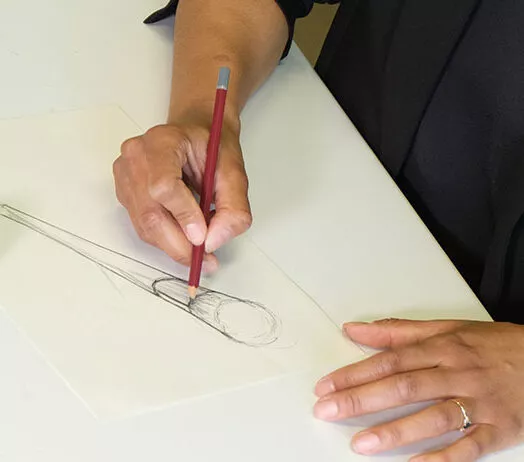 Designer dessinant un pinceau cosmétique à main levée sur une table de travail blanche