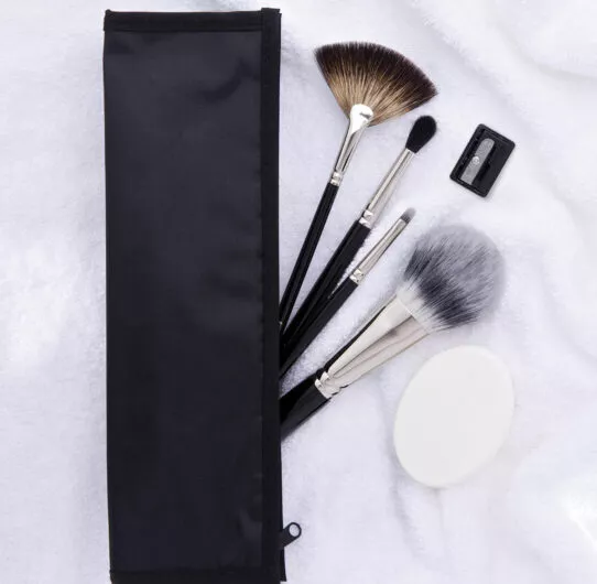Trousse noire ouverte avec pinceaux de maquillage et accessoires disposés sur une serviette blanche