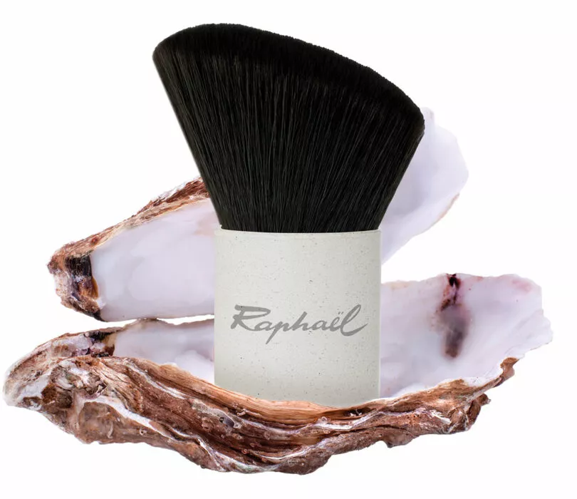 Eco-designed kabuki brush made from oyster shell powder, presented inside an open oyster shell