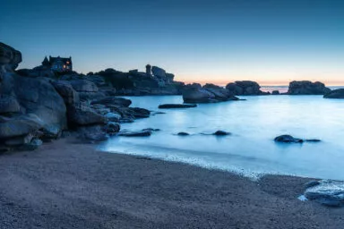 Paysage côtier de Bretagne au crépuscule, avec maison et phare sur les rochers