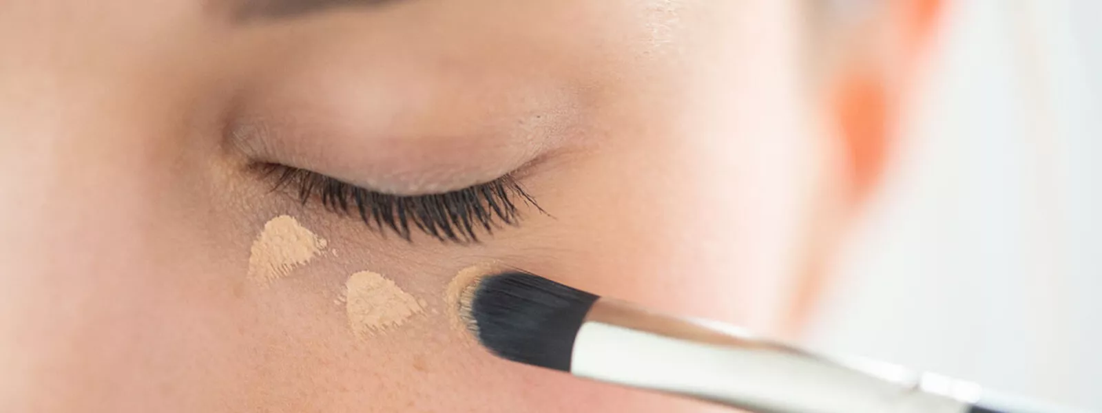 Close-up of a Raphaël concealer brush blending makeup under the eye