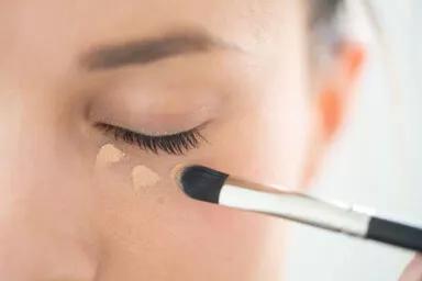 Close-up of a Raphaël concealer brush blending makeup under the eye
