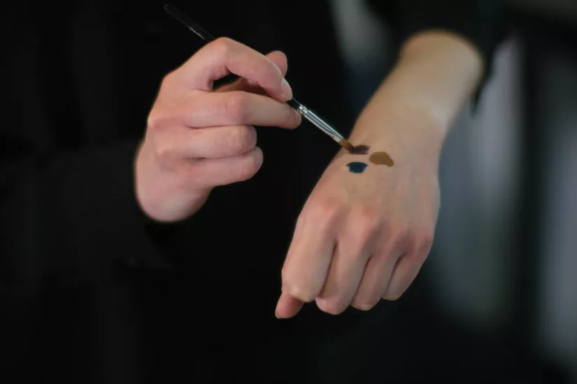 Application de maquillage testée sur la main à l’aide d’un pinceau Raphaël pour vérification des teintes